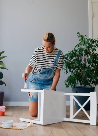 Téléchargez les photos : Femme Upcycling meubles dans à la maison peinture chaise en bois - en image libre de droit