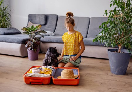 Téléchargez les photos : Adolescent fille valise d'emballage à la maison. Concept de voyage - en image libre de droit