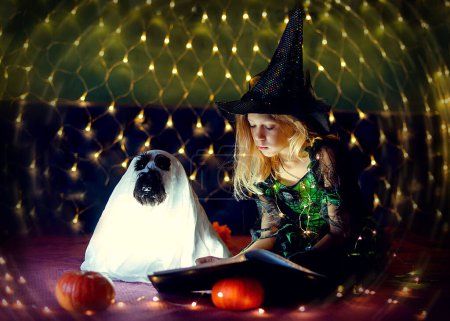 Foto de Niña con disfraz de bruja en truco o trato de Halloween. El chico juega con el perro. Los niños celebran Halloween. Truco o trato familiar - Imagen libre de derechos