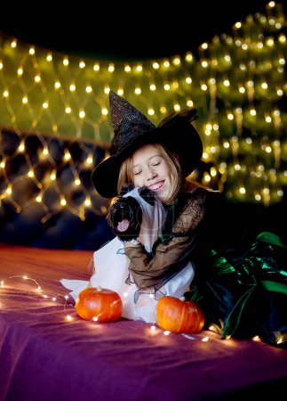 Foto de Niña divertida niño en traje de Halloween de bruja y sombrero negro decorado con calabazas con perro en capa de Drácula - Imagen libre de derechos