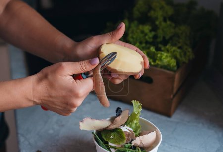 Photo for Hands of cook cut peel of raw potatoes , peeler, put food waste in separate container for further processing. Zero waste, using organic waste for compost - Royalty Free Image