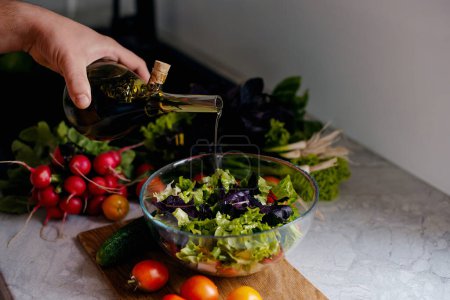 Photo for Hand pours freshly prepared salad from a glass bottle with olive oil. Vegetarian food concept - Royalty Free Image