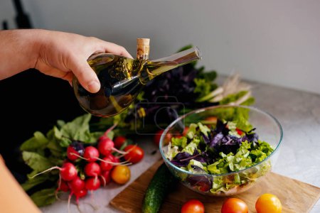 Foto de La mano vierte ensalada recién preparada de una botella de vidrio con aceite de oliva. Concepto de comida vegetariana - Imagen libre de derechos