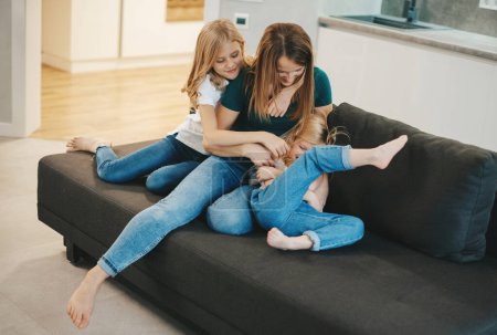 Téléchargez les photos : Famille à la maison s'amuser. mère et filles riant sur le canapé - en image libre de droit