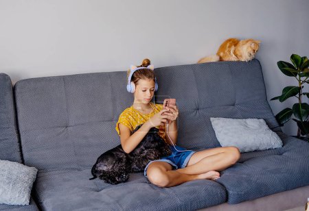 Photo for Girl in plaid listening music in headphones, sitting on sofa. - Royalty Free Image