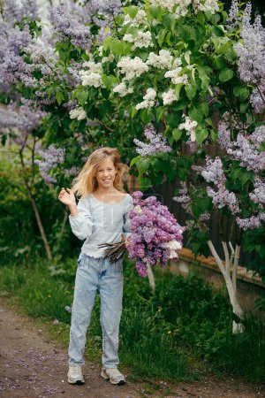 Foto de Hermosa joven con un ramo de lilas, una chica en lilas, lilas en primavera. Chica joven posando con un ramo de lila - Imagen libre de derechos