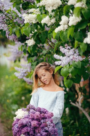 Foto de Hermosa joven con un ramo de lilas, una chica en lilas, lilas en primavera. Chica joven posando con un ramo de lila - Imagen libre de derechos