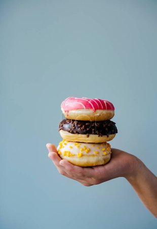 Photo for A hand holding a stack of three delicious donuts, a popular staple food and fast food choice. Enjoy these baked goods as a sweet treat or dessert - Royalty Free Image