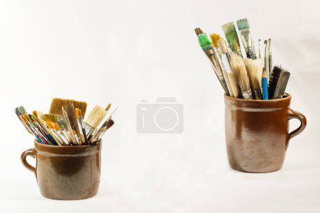 Photo for Artistic brushes and painting tools in old clay/ceramic pots on white neutral background. - Royalty Free Image