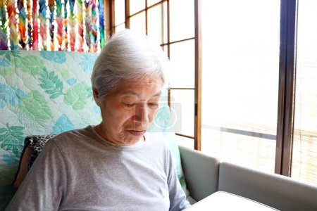 Téléchargez les photos : Femme âgée aux cheveux gris assise sur un lit d'allaitement inclinable et regardant une table - en image libre de droit