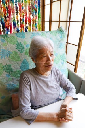 Téléchargez les photos : Femme âgée avec les cheveux gris assis sur un lit d'allaitement inclinable et regardant droit devant - en image libre de droit