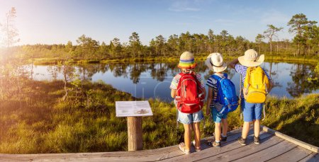 Children standing on the boardwalk on bog and looking on the lake. Concept of hiking, vacation and friendship.