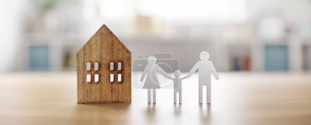 Figurines of family and wooden house standing on the table indoors. Concept of buying and renting new real estate.