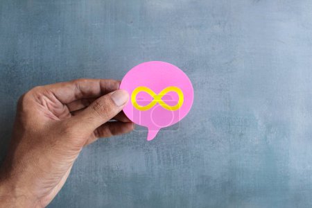Photo for A close-up photo of a hand holding a pink speech bubble with a gold infinity symbol on it. - Royalty Free Image