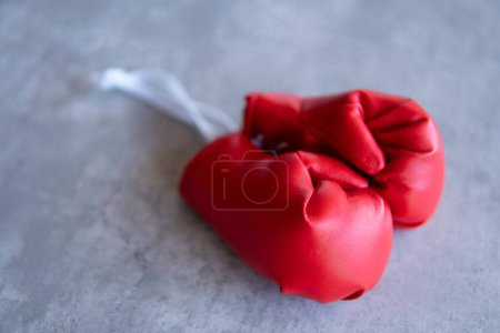 Ein Nahaufnahme-Bild roter Boxhandschuhe, die auf einer grauen Leinwandoberfläche ruhen. Die Handschuhe liegen nebeneinander, wobei die Schnürsenkel einander zugewandt sind.