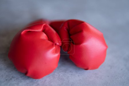 Ein Nahaufnahme-Bild roter Boxhandschuhe, die auf einer grauen Leinwandoberfläche ruhen. Die Handschuhe liegen nebeneinander, wobei die Schnürsenkel einander zugewandt sind.