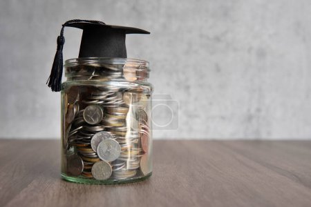 Photo for Glass jar filled with coins and a graduation cap on top of it. Copy space for text. Education savings concept. - Royalty Free Image