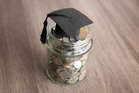 Glass jar filled with coins and a graduation cap on top of it. Copy space for text. Education savings concept.