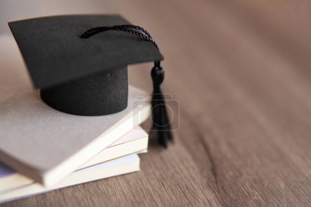 Graduation cap on top of stack of books on a wooden table. Copy space for text. Education concept.