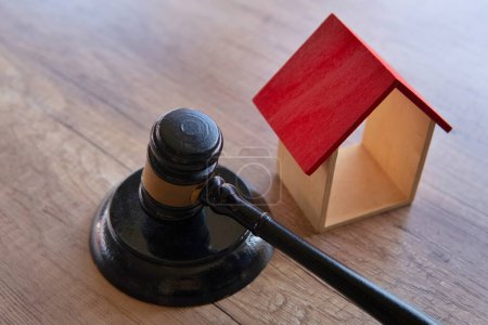 Closeup image of gavel next to miniature wooden house. House auction, expropriation and eviction concept.