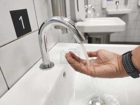 Nahaufnahme eines Mannes, der sich mit einem berührungslosen Wasserhahn die Hände wäscht.