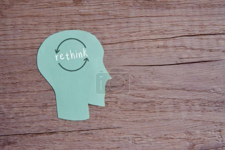 A conceptual image with the word "rethink" written across a paper cutout head on wooden table with copy space. 
