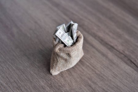 Closeup image of burlap sack overflowing with stacks of U.S. dollar bills with copy space. Prosperity, wealth, profit concept.