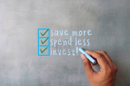 Hand writing on chalkboard text SAVE MORE, SPEND LESS, INVEST. Financial concept.