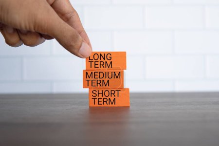 Hand pick wooden cube with text LONG TERM on blue background with copy space. Investment concept.
