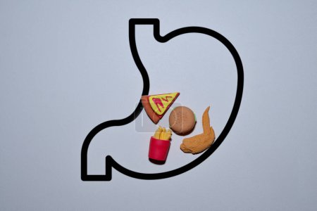 Conceptual image of full stomach with a variety of fast food like pizza slice, hamburger, fries, and chicken wings. Unhealthy eating, bad eating habits concept.