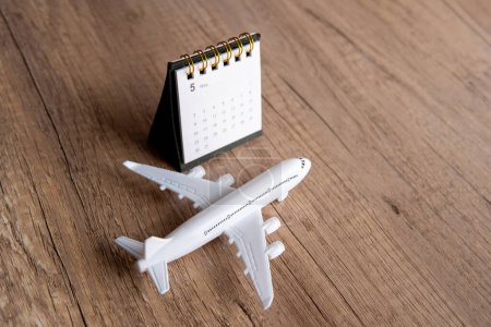 Toy airplane on a wooden table next to a calendar. Copy space for text. Flight reschedule, checking flight availability concept.