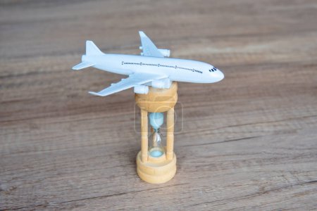 Toy airplane on a wooden table next to a hourglass. Copy space. Flight delay, waiting concept.