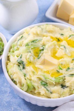 Photo for Traditional homemade Irish dish Colcannon or mashed potato with green cabbage and butter, served in white bowl, spring onion and butter on light blue concrete background, St Patrick day food, vertical - Royalty Free Image