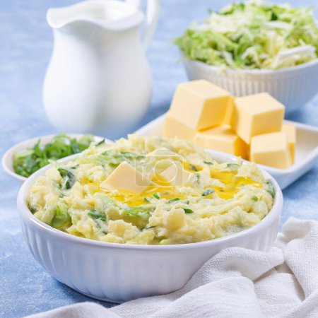Photo for Delicious homemade Irish dish Colcannon or mashed potato with green cabbage and butter, served in white bowl, spring onion and butter on light blue concrete background, St Patrick day food, square - Royalty Free Image