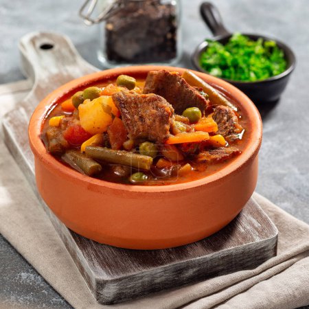 Vegetable beef stew with potato, green beans, carrot, celery, peas and corn, in ceramic bowl, square format