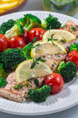 Baked salmon fillet with broccoli and tomato on a plate, salmon steak with vegetables, vertical, closeup