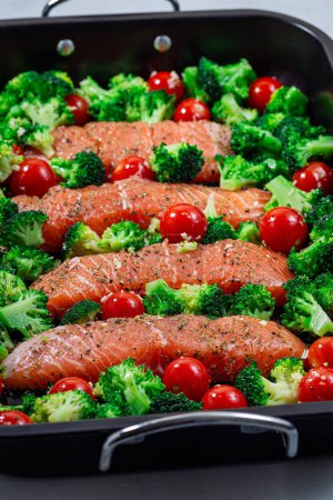 Ready to bake raw salmon fillet with broccoli and tomato on a frying tray, vertical closeup