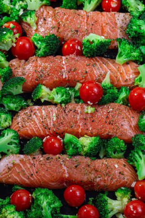 Ready to bake raw salmon fillet with broccoli and tomato on a frying tray, vertical, top view, closeup