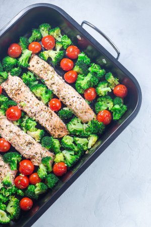 One pan dish, baked salmon fillet with broccoli and tomato on a frying tray, vertical, top view