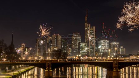 Silvester mit Feuerwerk über der Skyline von Frankfurt - Main bei Nacht an einem kalten Wintertag mit bunten Spiegelungen im Wasser.