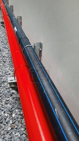 Téléchargez les photos : Pipeline horizontale de couleur noire et rouge installée le long du mur du bâtiment, montrant le système de conception d'utilité technique, les activités de construction, la direction du flux - en image libre de droit