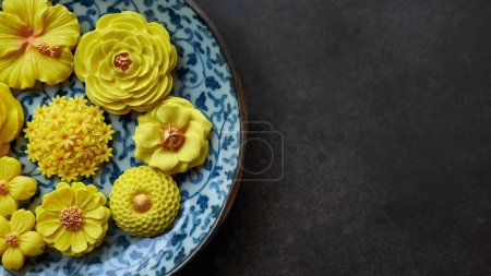 Thai-Dessert in verschiedenen blumenförmigen, warmen Farbton, gelbe Mango-Geschmack in antiken Musterteller, Sam Pan Nee traditionelle thailändische Kunsthandwerk-Snack im dunklen Hintergrund 