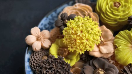 Thai dessert in various flower shaped, warm color tone, orange, chocolate and mango flavor, Sam Pan Nee traditional Thai handcraft snack in Dark background, Royal famous Thai sweets