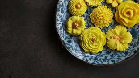 Postre tailandés en forma de flor, tono de color cálido, sabor de mango amarillo en placa de patrón antiguo, Sam Pan Nee snack tradicional de artesanía tailandesa en fondo oscuro 