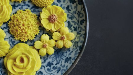 Thai dessert in various flower shaped, warm color tone, yellow mango flavor in antique pattern plate, Sam Pan Nee traditional Thai handcraft snack in Dark background 