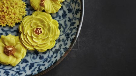 Thai dessert in various flower shaped, warm color tone, yellow mango flavor in antique pattern plate, Sam Pan Nee traditional Thai handcraft snack in Dark background 