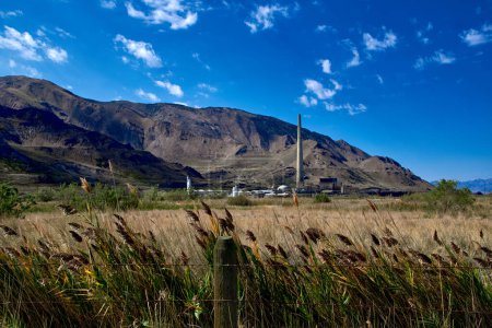 Foto de Mirando a través de un campo de hierba en una planta de fundición de cobre y es 1,215 pies de altura pila de humo, con las montañas Tooele en el fondo, al oeste de Salt Lake City, Utah. - Imagen libre de derechos
