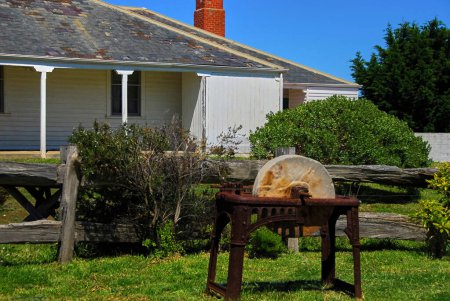 An old grindstone stands in front of a old farmhouse in need of repairs in rural Victoria, Australia.