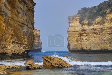 Dramatic cliffs tower above the entrance to a small ocean bay as waves crash over the rocks on the beach on the southern coast of Victoria, Australia.