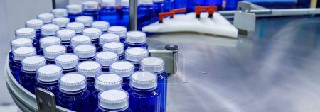 Foto de Botella de plástico azul en la línea de producción de cinta transportadora en la máquina de llenado en la fábrica médica. fabricación farmacéutica. - Imagen libre de derechos